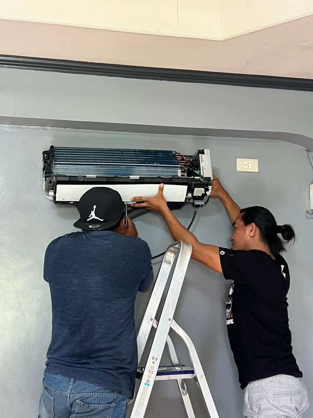 Two technicians working on an open wall-mounted indoor aircon unit